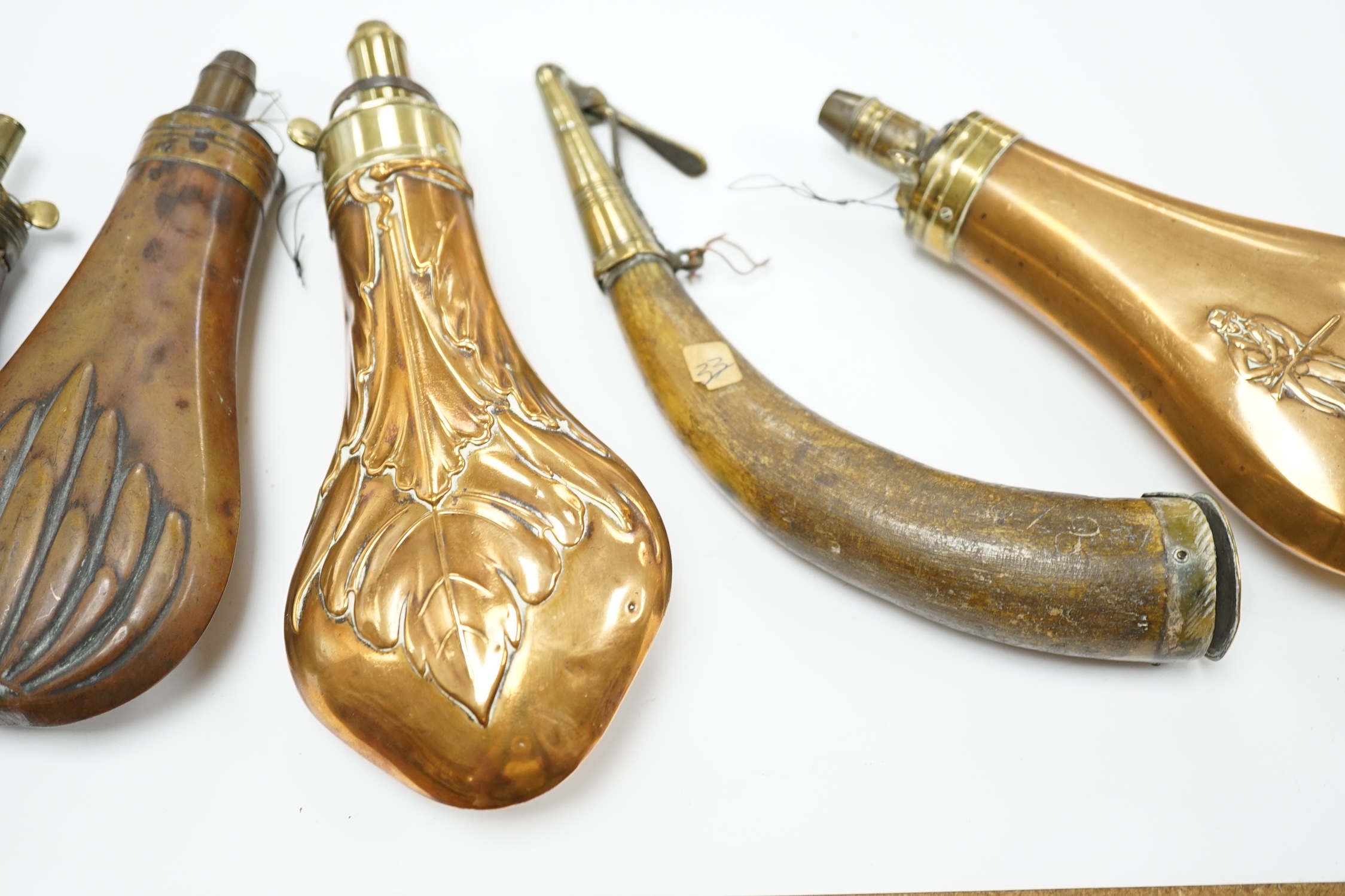 Five 19th century powder flasks; three copper and brass flasks, two with embossed decoration to the bodies, a leather covered flask and a horn Royal Artillery priming horn. Condition - poor to fair